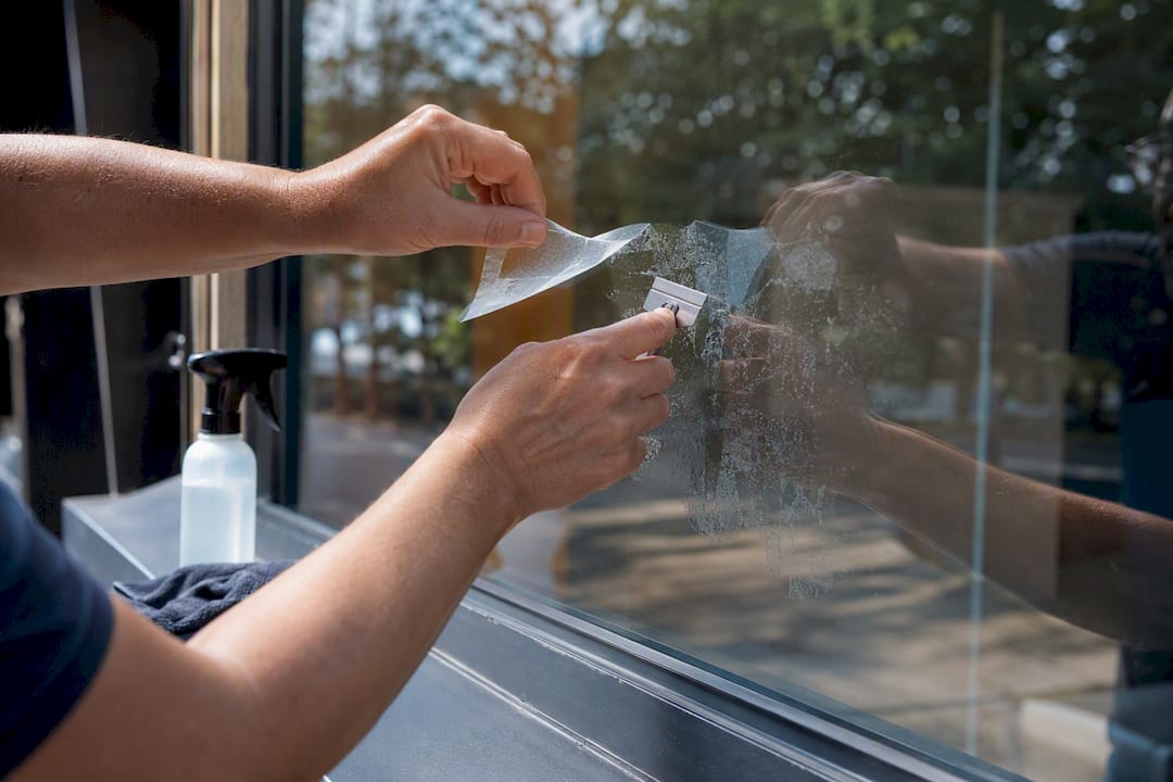 Hands scraping vinyl decal from storefront glass