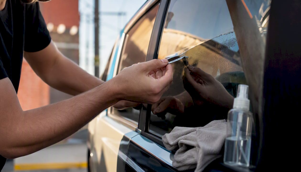 Hand removing rear window decal with razor blade