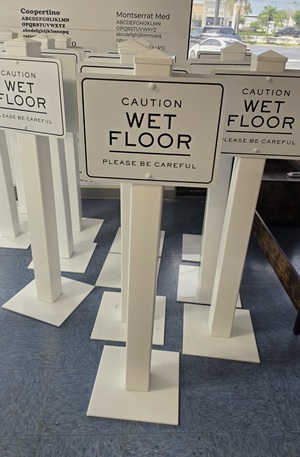 Row of white “Caution Wet Floor” signs with base stands, indoors.