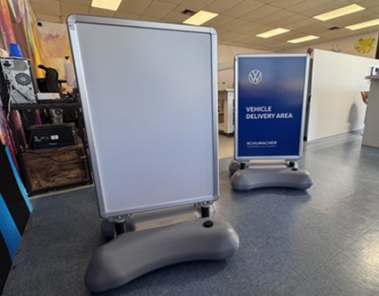 Two wheeled display boards in a bright indoor space; one blank, one sign reads Vehicle Delivery Area.